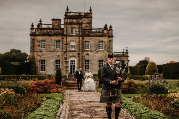 A traditional Scottish piper leading a bride and groom through the Italian Gardens